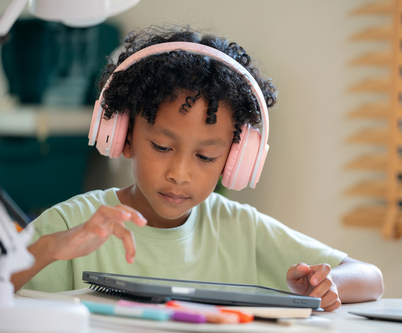 donker jongetje met donker krullend haar en een roze koptelefoon op kijkt naar een ipad scherm
