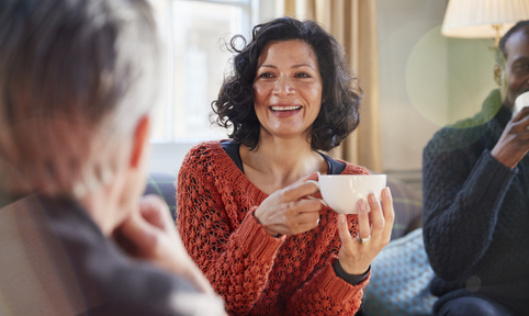 vrouw heeft een kop thee vast en lacht naar ander persoon
