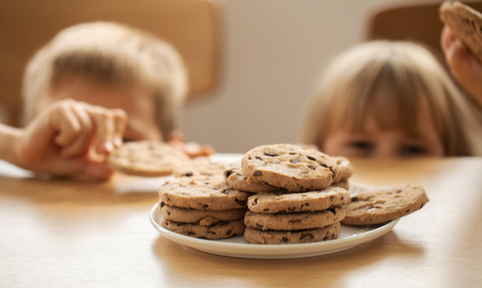 2 kinderen met blond haar steken uit boven een tafel waar een bord met koekjes opstaat