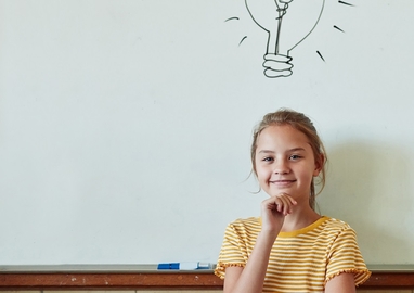 meisje staat voor een schoolbord waarop een gloeilamp is getekend