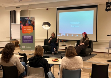 Marjolein en Bianca zitten naast elkaar voor een groep ouders